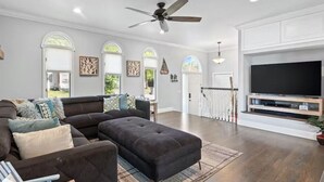 A spacious living room with a large sectional sofa, a flat-screen TV, and a ceiling fan.