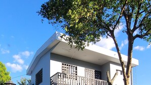 A modern two-story house with a balcony, surrounded by well-maintained greenery and a clear blue sky.