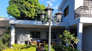 A pathway leading to a building with a white facade, a large tree, and a street lamp.