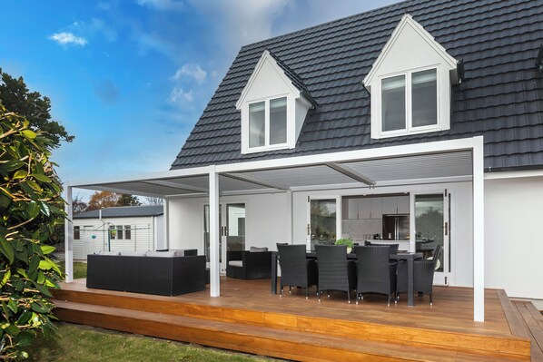Ein modernes Haus mit überdachter Terrasse, Essbereich und durch Glastüren einsehbarer Küche.