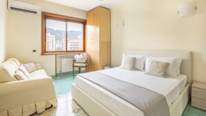 A hotel room with a large bed, a sofa, a wooden wardrobe, and a window with a city view. - Family Home with terrace & view in Sorrento Center (Sorrento)