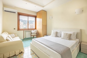 A hotel room with a large bed, a sofa, a wooden wardrobe, and a window with a city view. - Family Home with terrace & view in Sorrento Center (Sorrento)