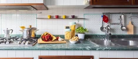 A kitchen with wooden cabinets, a gas stove, a sink, and various kitchen items on the countertop.