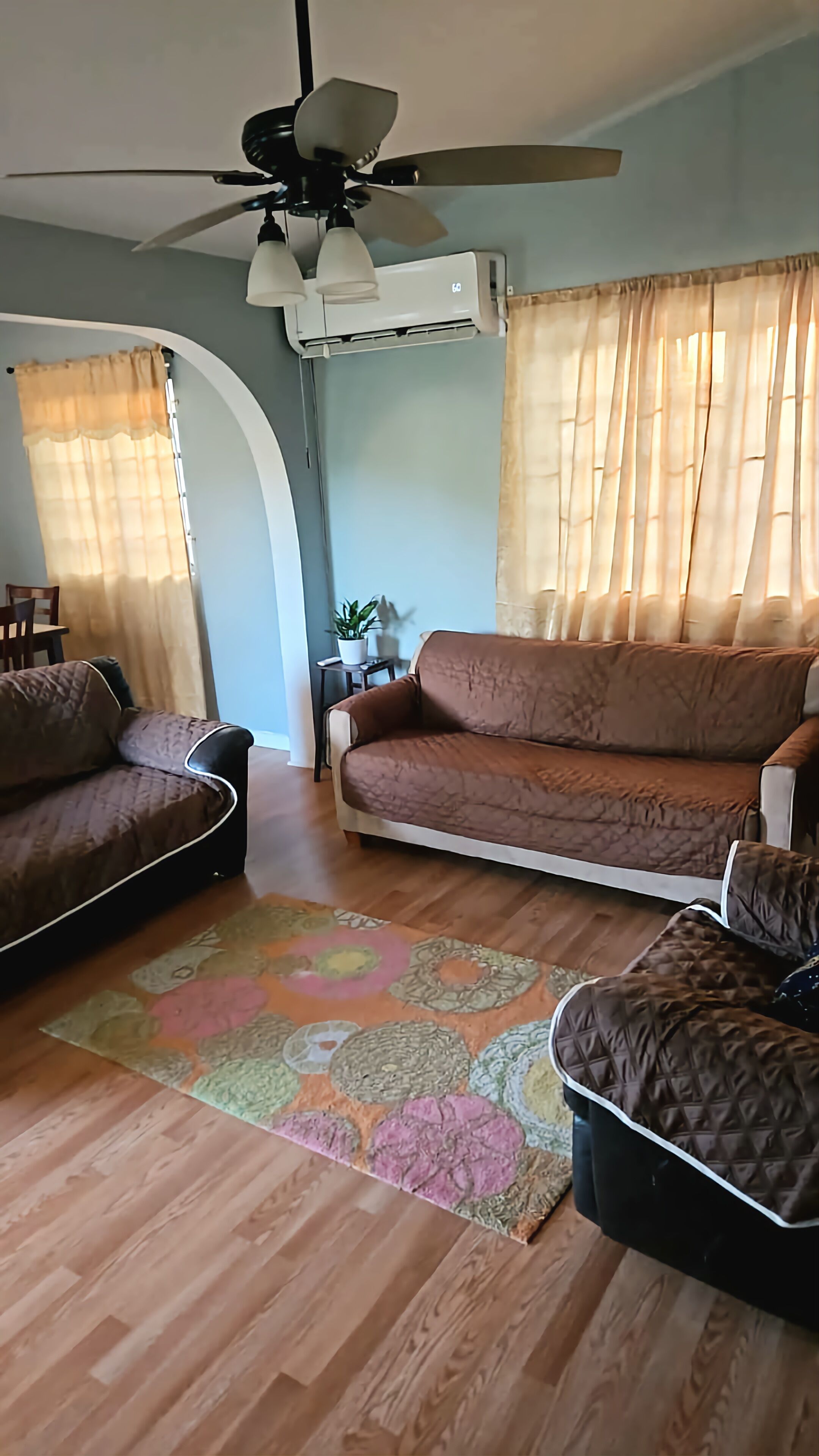 Un salon avec un canapé marron, un tapis à motifs et un ventilateur de plafond.