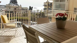 Une terrasse avec une table et des chaises en bois, un pot de fleurs et un auvent à rayures.