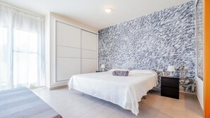 Una habitación de hotel con una cama, una mesita de noche, una lámpara y un ventanal grande con cortinas.
