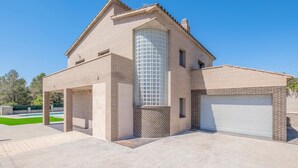 Una casa moderna de dos pisos con una alta torre cilíndrica de vidrio, un garaje cubierto y un césped cuidado.