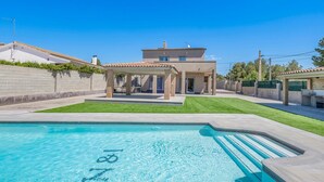 Una casa moderna con piscina, un porche cubierto y un césped cuidado.