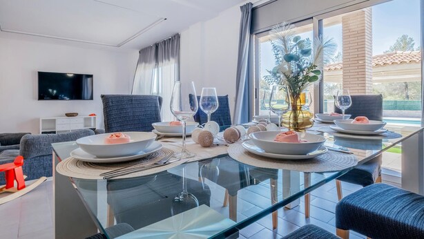 Un comedor moderno con una mesa de vidrio, sillas tapizadas en azul y vistas al exterior a través de grandes ventanales.