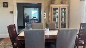 A dining area with a table, chairs, a cabinet with glass doors, and a hallway leading to another room.