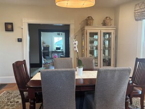 Een eethoek met een tafel, stoelen, een kast met glazen deuren en een gang naar een andere kamer.
