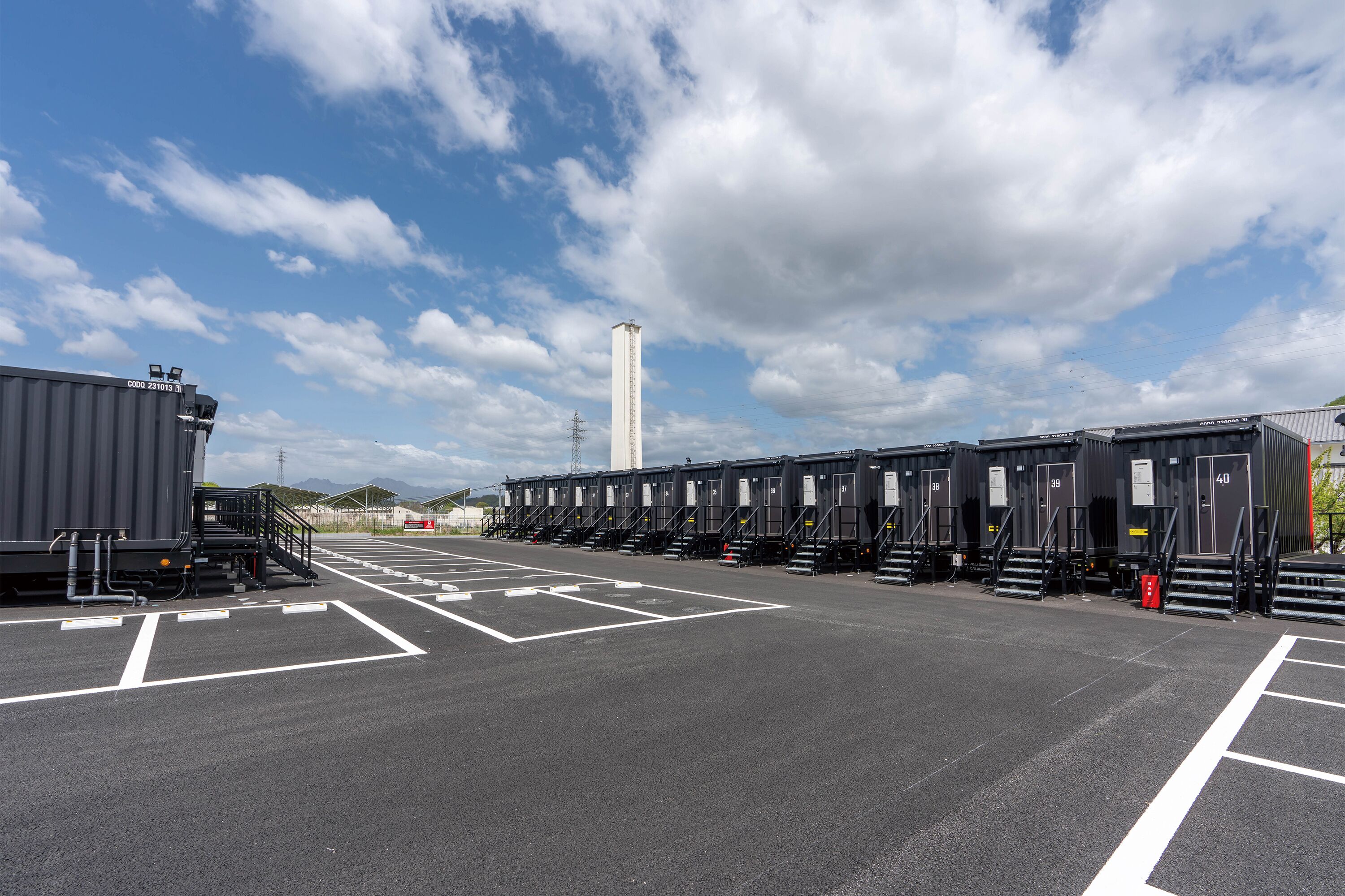 A parking lot with rows of portable toilets and a tall white structure in the background.