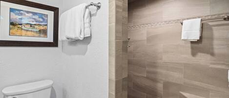 A bathroom with a toilet, a framed landscape painting, and a shower area with a tiled floor.