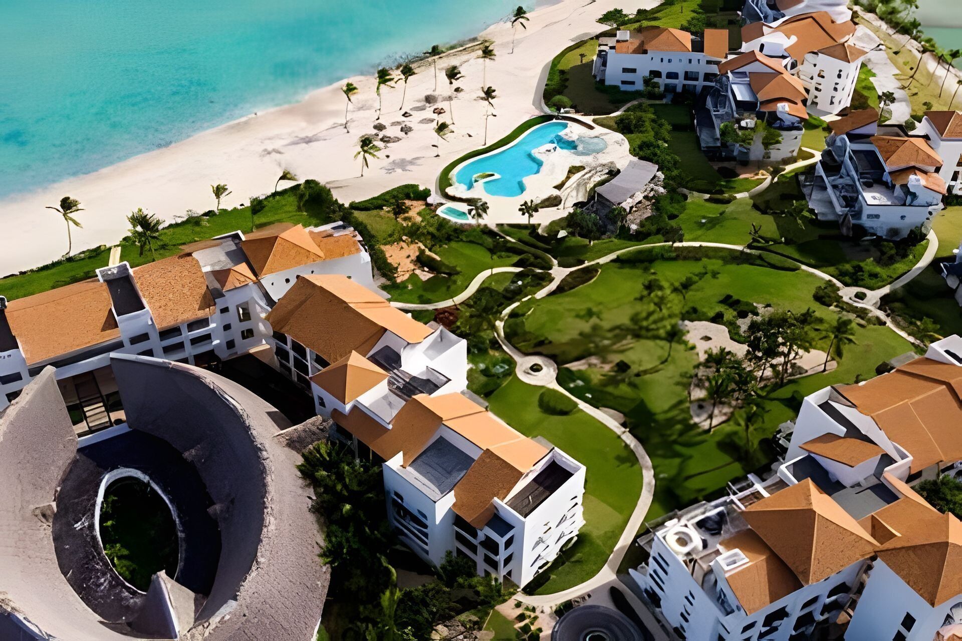 An aerial view of a resort with multiple buildings, a beach, and a swimming pool.