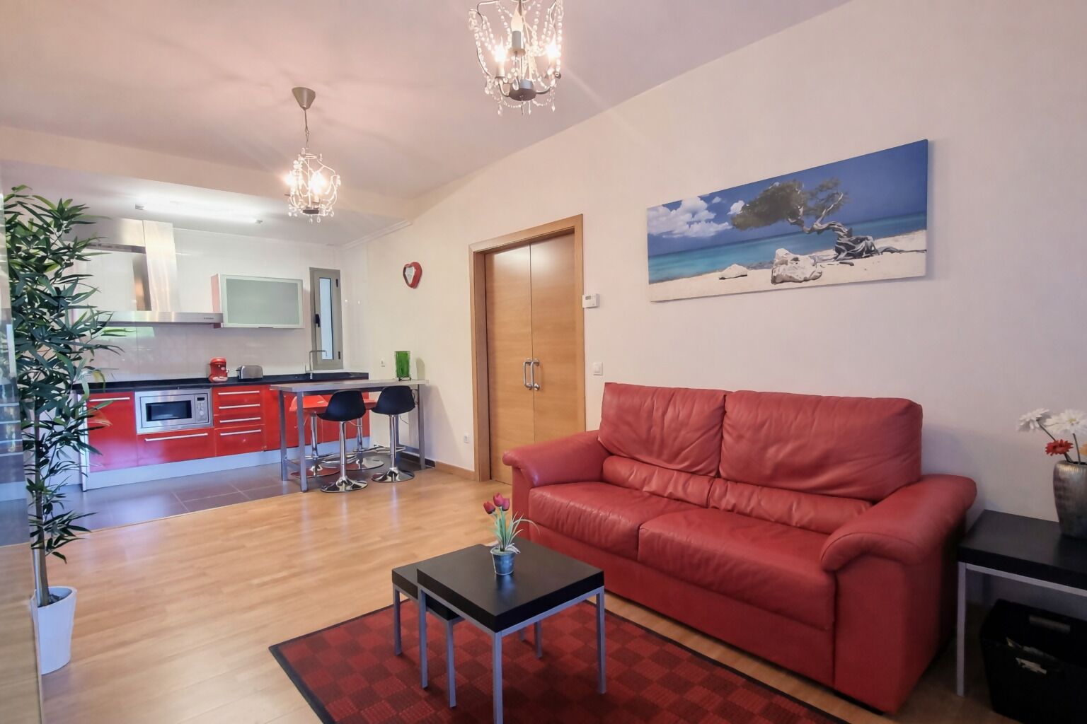 A living room with a red sofa, a small table, and a painting of a beach scene.