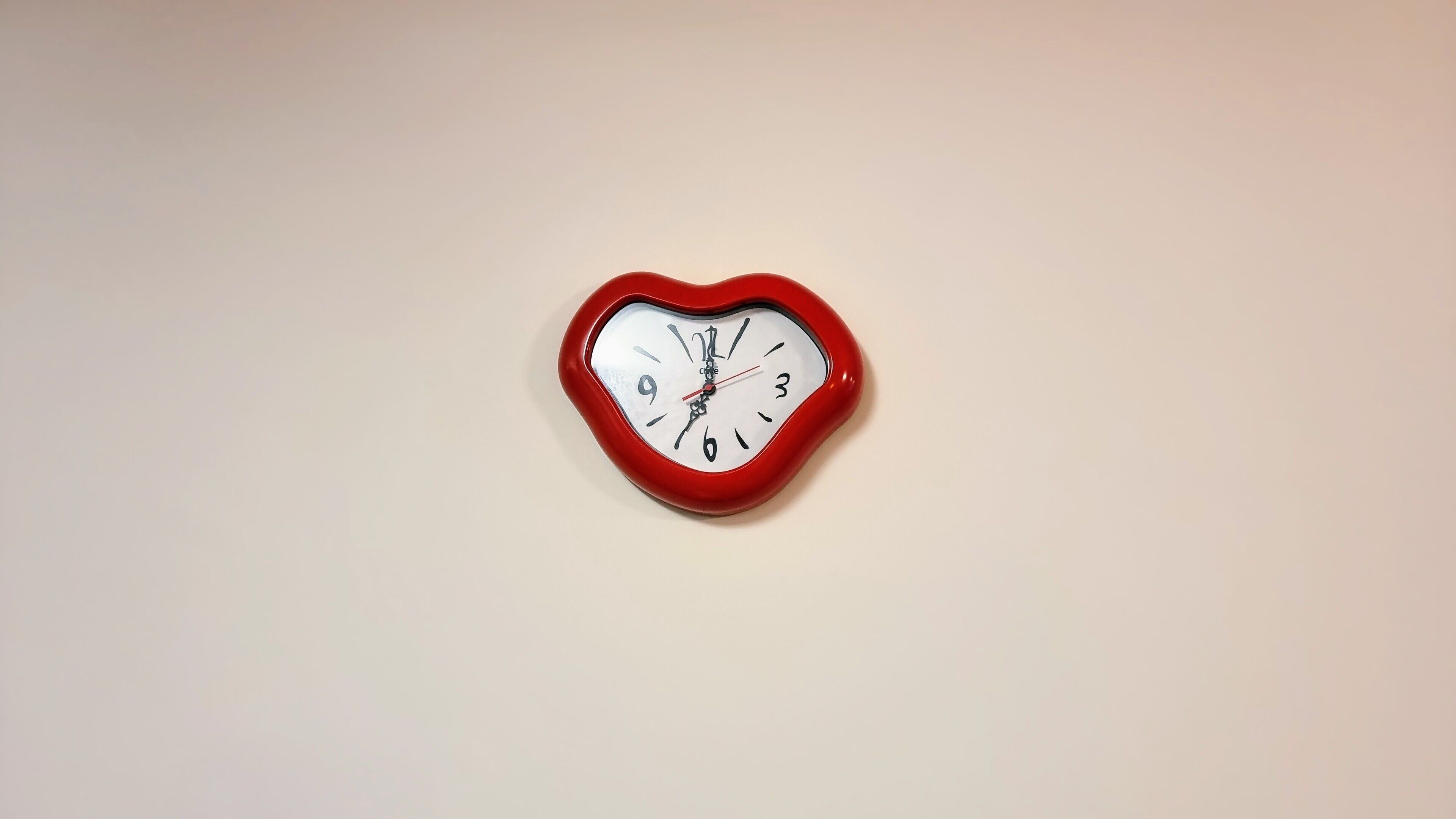 A heart-shaped clock with a white face and black numbers, mounted on a plain wall.