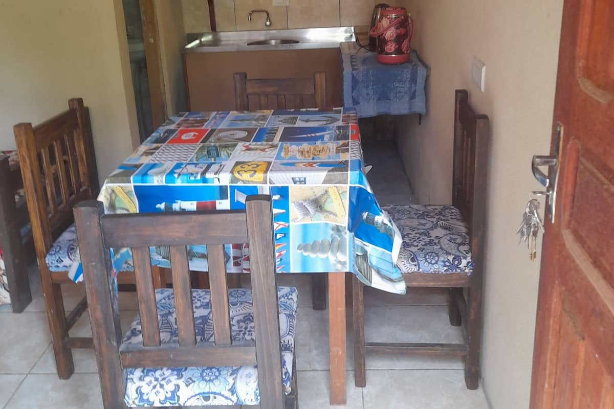 A compact kitchen with a tiled backsplash, a sink, and a countertop. There is a table with a patterned tablecloth and wooden chairs.