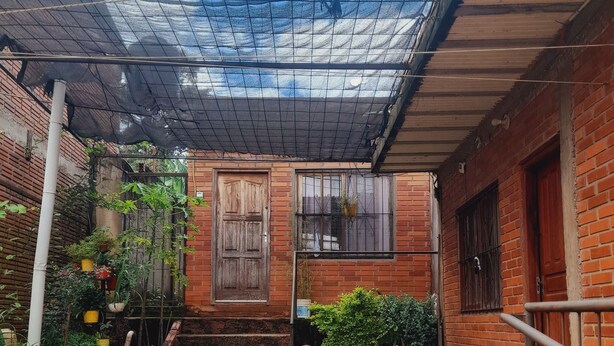 A courtyard with a brick building, a metal fence, and steps leading to a door. - Valeria  (Puerto Iguazú)