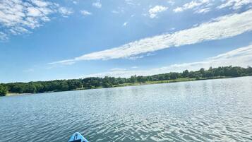 Un kayak blu su acqua calma, con cielo sereno e alberi in lontananza.