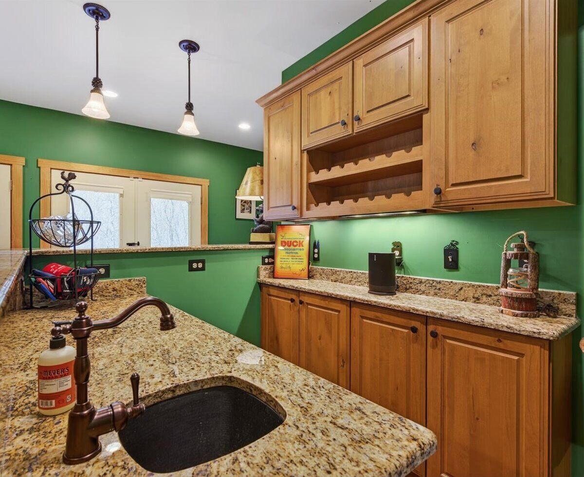 A kitchen with granite countertops, wooden cabinets, a black sink, and pendant lighting.