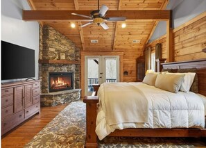 Um quarto com lareira de pedra, teto de madeira, cama, penteadeira e televisão.
