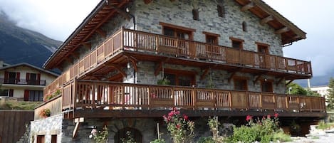 Un immeuble en pierre à plusieurs étages, doté de balcons en bois et d’une allée gravillonnée.