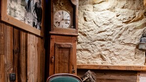 A wooden chair with a green cushion, a wooden cabinet with a clock, and a stone wall. - Apartment 'L'erelaz' with Mountain View and Wi-Fi (SOLLIERES SARDIERES)