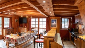 A cabin interior with a wooden ceiling, a dining table with chairs, a kitchen area, and a large window. - Apartment 'L'erelaz' with Mountain View and Wi-Fi (SOLLIERES SARDIERES)
