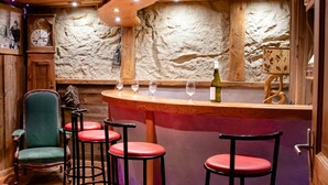 A bar area with wooden bar stools, a clock, and a stone wall. - Apartment 'L'erelaz' with Mountain View and Wi-Fi (SOLLIERES SARDIERES)