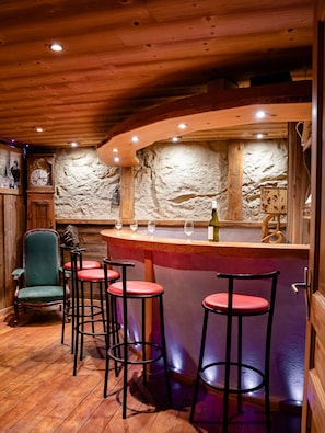 A bar area with wooden bar stools, a clock, and a stone wall.