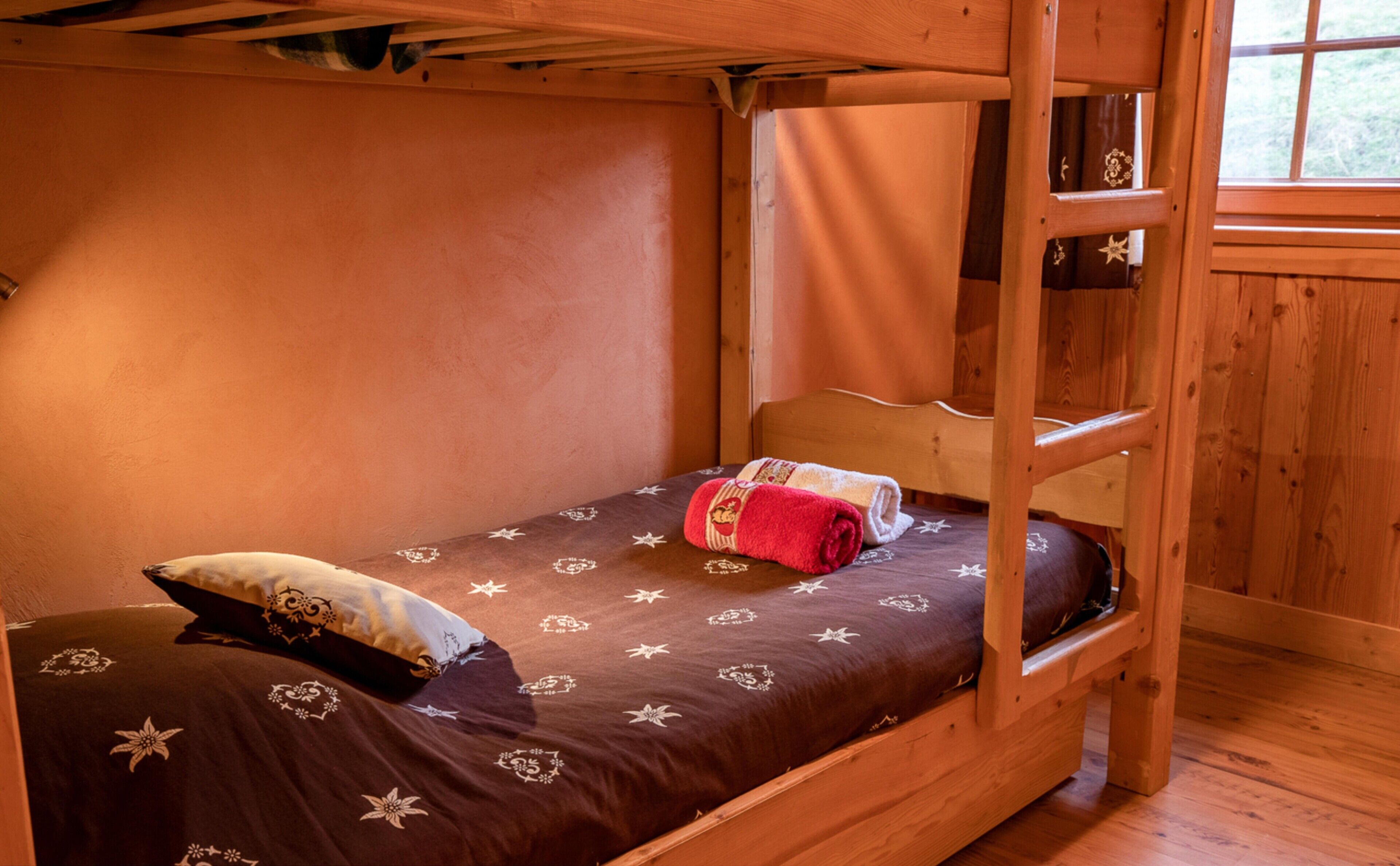 Una cama litera con una colcha estampada, una toalla enrollada y un almohadón.