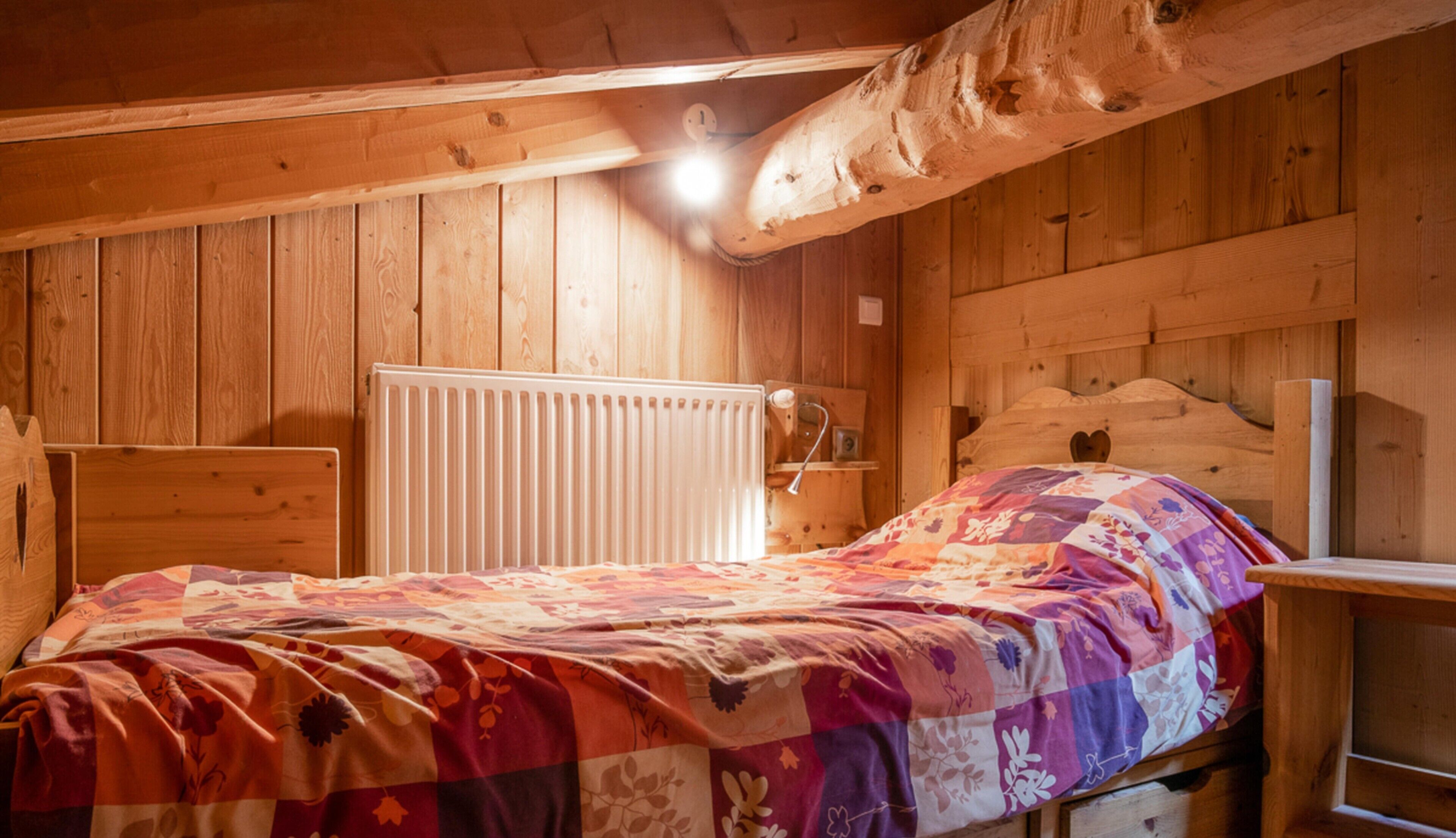 Una habitación de cabaña de madera con una cama, un radiador y un cabecero de madera.