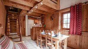Een houten hut van binnen met een eethoek, keuken en een raam met gordijnen.
