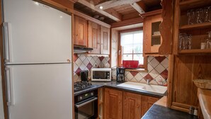 Een keuken met houten kastjes, een witte koelkast, een magnetron, een fornuis en een spoelbak.