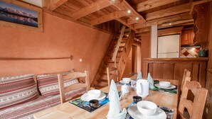 Een rustiek houten interieur met een eettafel gedekt voor vier personen, een houten bank met kussens, een trap en een keukenhoek.