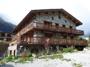 Ein mehrstöckiges Steinhaus mit hölzernen Balkonen und einer Auffahrt mit Kies.