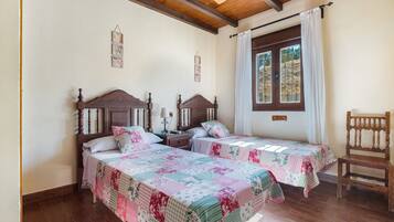 A room with two wooden beds, a wooden chair, a ceiling fan, and a window with curtains.