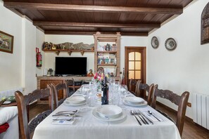 A dining room with a long table set for a meal, wooden chairs, a television, and a bookshelf.