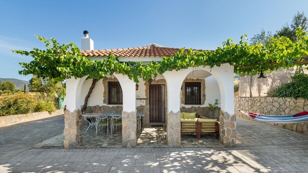 Een villa met een overdekt terras, stenen zuilen en een hangmat.