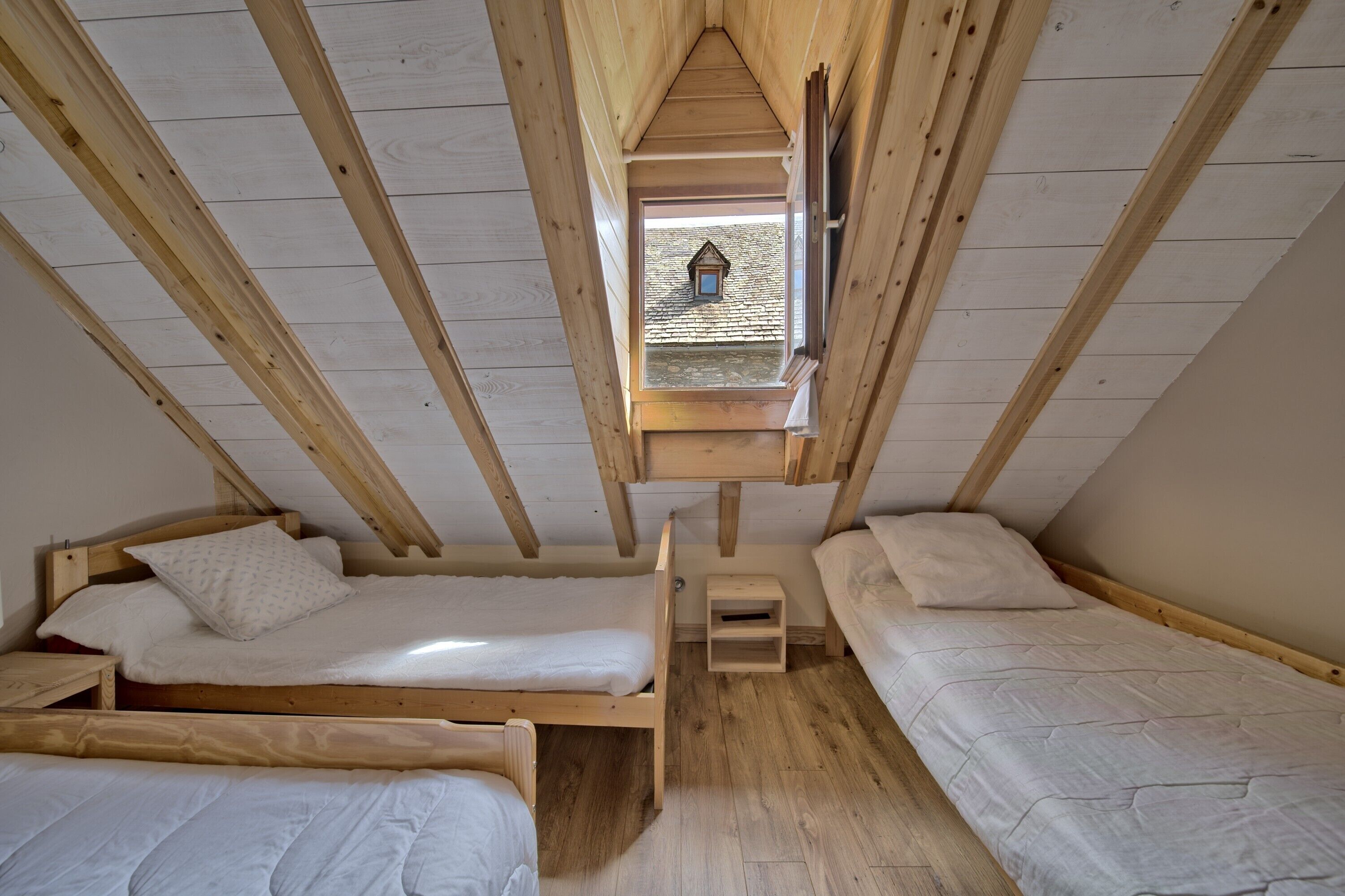 A dormitory-style room with three wooden bunk beds, a small wooden stool, and a skylight.