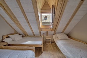 Une chambre de type dortoir avec trois lits superposés en bois, un petit tabouret en bois et une lucarne.