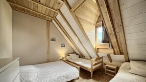 A room with a sloped ceiling, wooden beams, two beds with white bedding, a nightstand, and a small window.