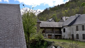 A rustic building with a stone facade, a balcony, and a mountainous backdrop.