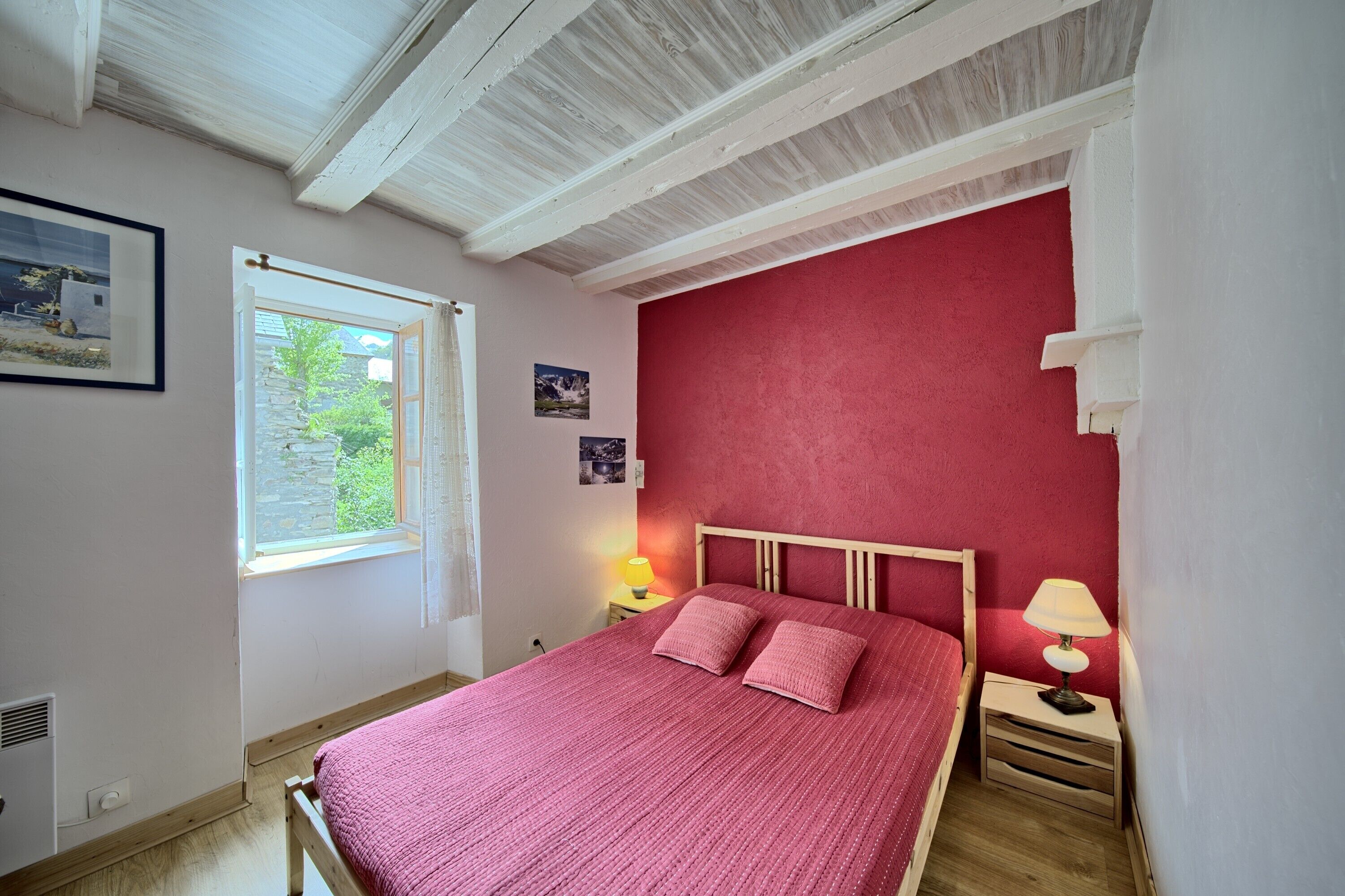 A bedroom with a wooden bed, a window with a view of greenery, and a red wall.