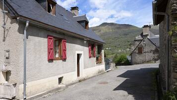 Una calle estrecha con edificios de piedra, contraventanas rojas y una montaña al fondo.