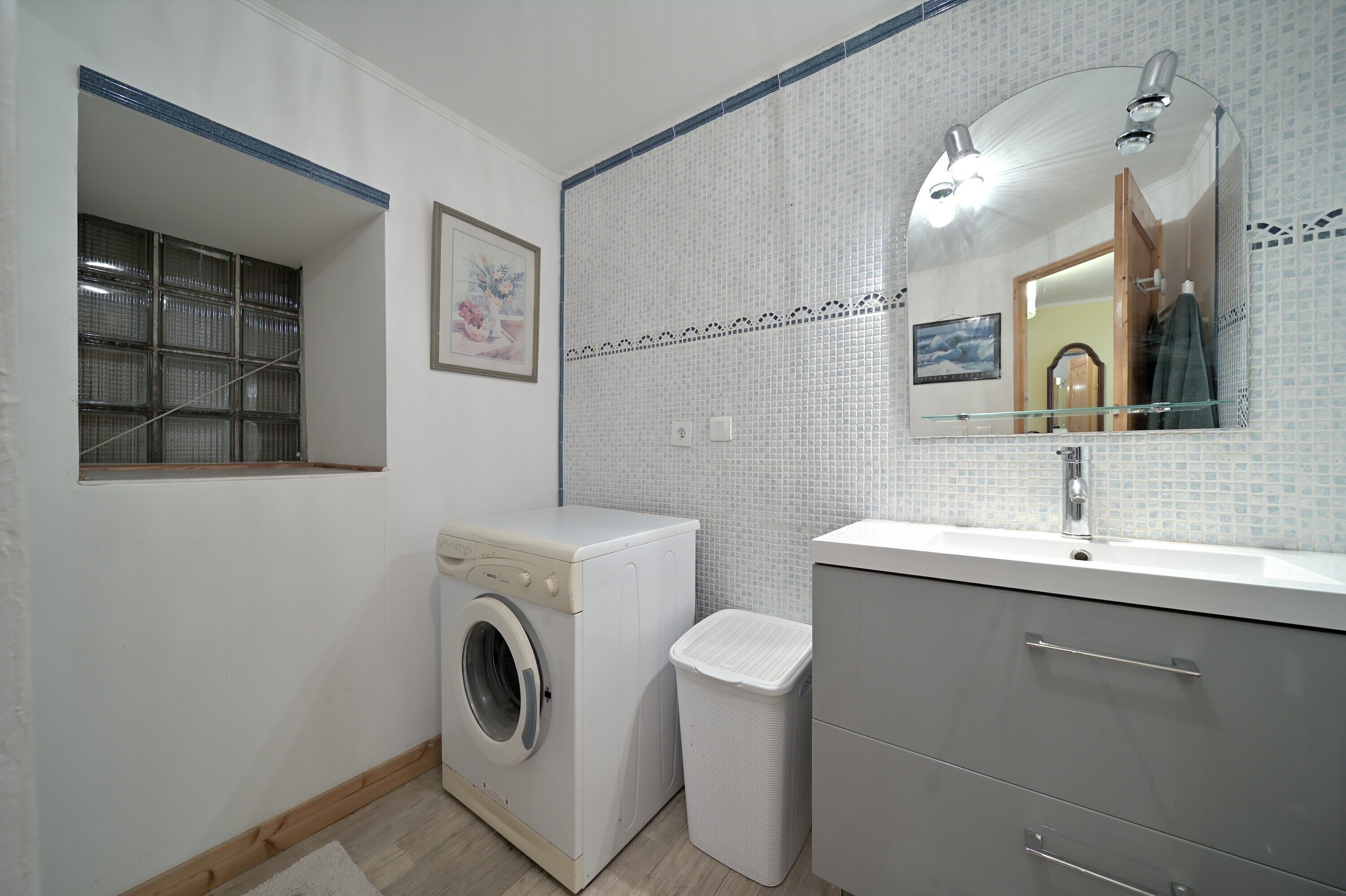 Casa de banho compacta com máquina de lavar, um lixo, uma pia com espelho e paredes em azulejo.