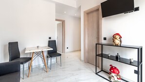 Moderni huone, jossa on taulutelevisio, ruokapöytä tuoleineen, sivupöytä hyllyineen ja ovi.