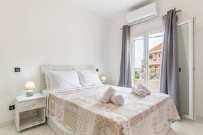 A bedroom with a bed, nightstand, lamp, and a view of buildings through a window.