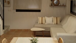 Un comedor con una mesa, sillas, una lámpara colgante, un sofá y un estante de pared.