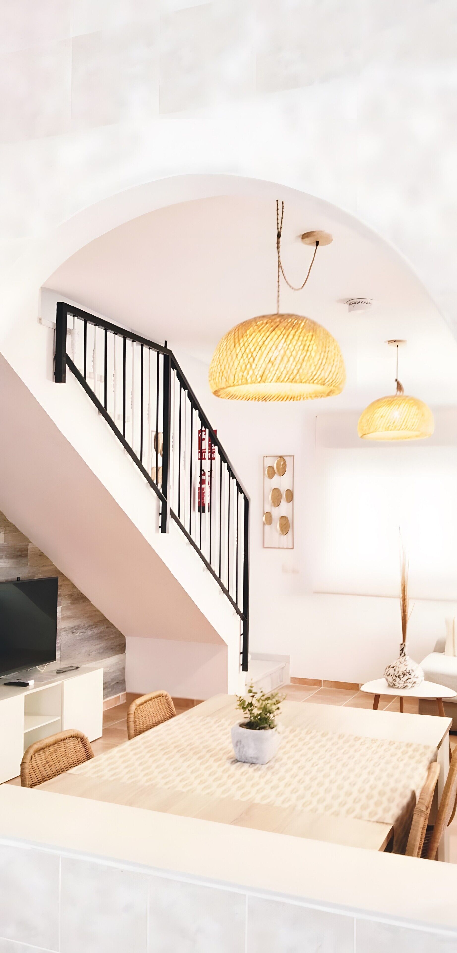 Un interior moderno con escalera, zona de comedor y lámparas colgantes.
